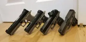 Handgun collection displayed on a polished wooden floor against a simple white door.