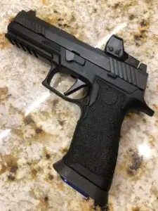 Modern semi-automatic handgun with red dot sight and tactical features on granite countertop.