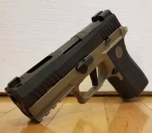 Semi-automatic handgun with tan and black design on a polished wooden floor.