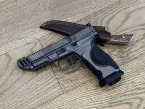 Handgun and knife on wooden surface, showcasing readiness and durability in outdoor gear.