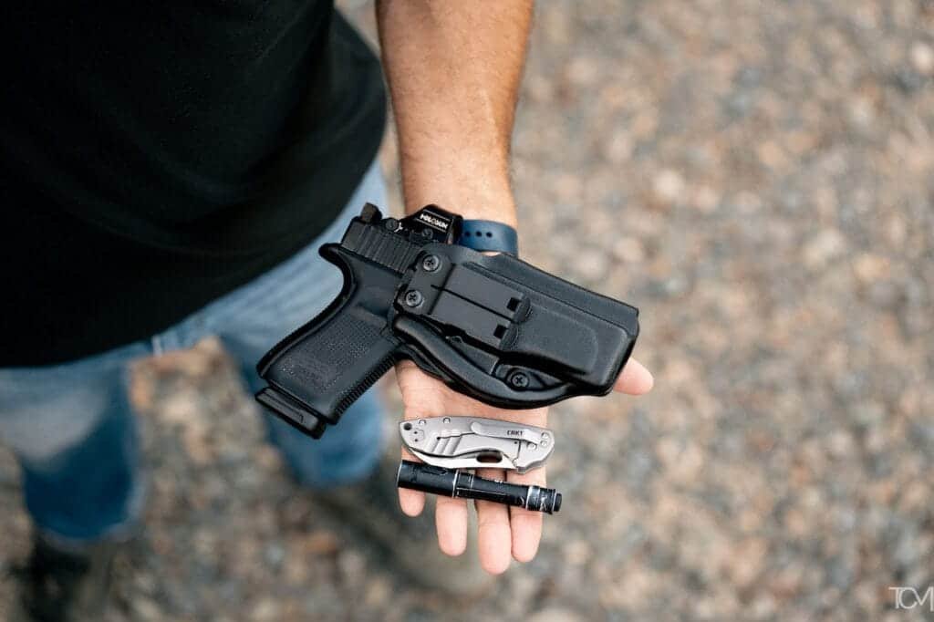 Man’s hand holds Glock 19 pistol, multi-tool, and flashlight, showcasing readiness for any situation.