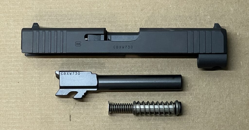 Glock 48 components for maintenance: slide, barrel, and recoil spring on a neutral background.